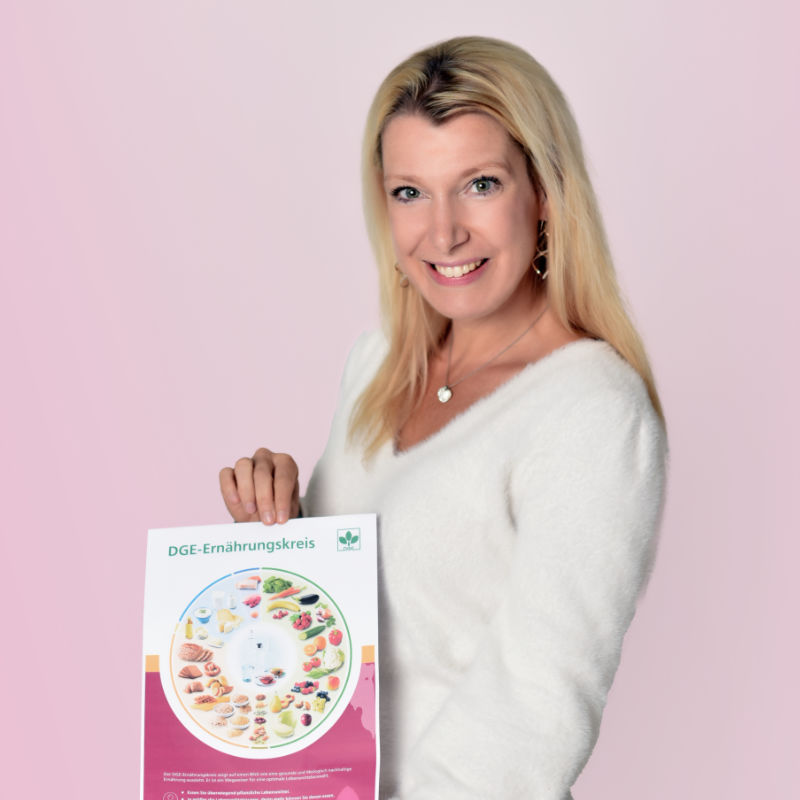 Porträt von Alexandra Groß, die ein Blatt mit dem DGE-Ernährungskreis in die Kamera hält.